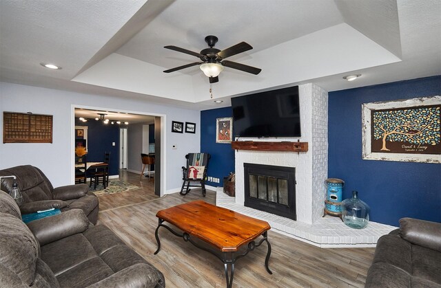 623 W Front St, Stuart, IA 50250 - living room featuring wood finished floors, ceiling fan, a tray ceiling, baseboards, and a brick fireplace