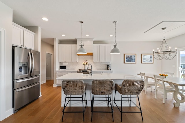 901 Cardinal Dr, Polk City, IA 50226 - kitchen with stainless steel fridge, light wood-style flooring, backsplash, white cabinets, and recessed lighting