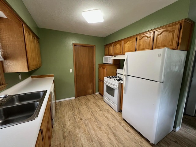 160 Bel Aire Dr, Waukee, IA 50263 - kitchen featuring white appliances, light wood finished floors, a sink, brown cabinets, and a textured ceiling