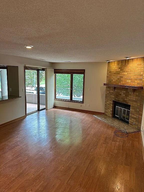 1100 50th St Unit 2102, West Des Moines, IA 50266 - unfurnished living room featuring a textured ceiling, baseboards, wood finished floors, and a brick fireplace