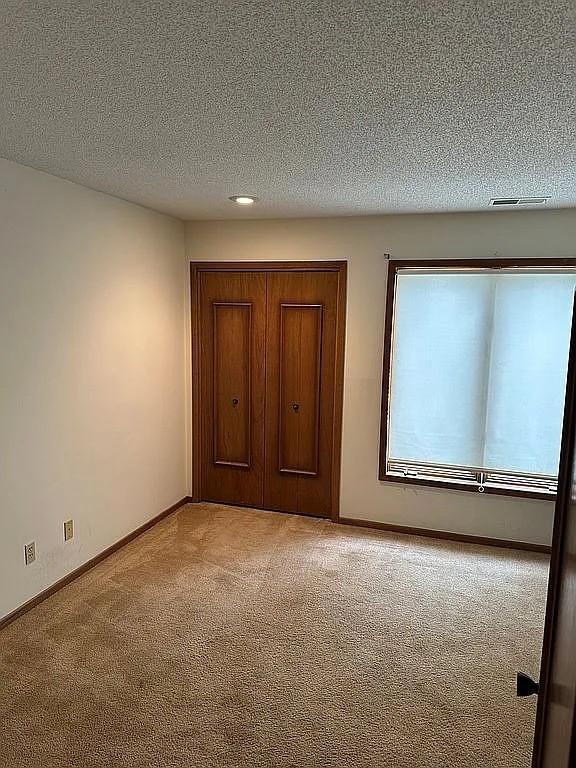 1100 50th St Unit 2102, West Des Moines, IA 50266 - unfurnished bedroom with light carpet, a closet, baseboards, and a textured ceiling