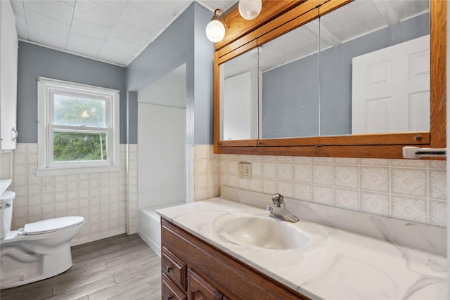 807 Center St, Grinnell, IA 50112 - full bath featuring toilet, tile walls, vanity, wood finished floors, and a wainscoted wall