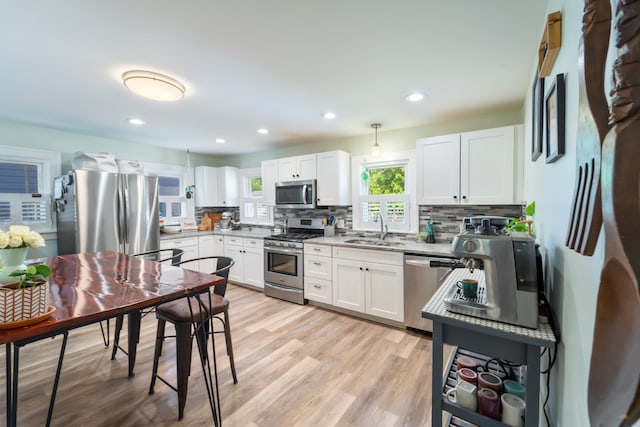 1516 57th Pl, Des Moines, IA 50311 - kitchen featuring stainless steel appliances, a sink, decorative backsplash, light wood-style floors, and white cabinets