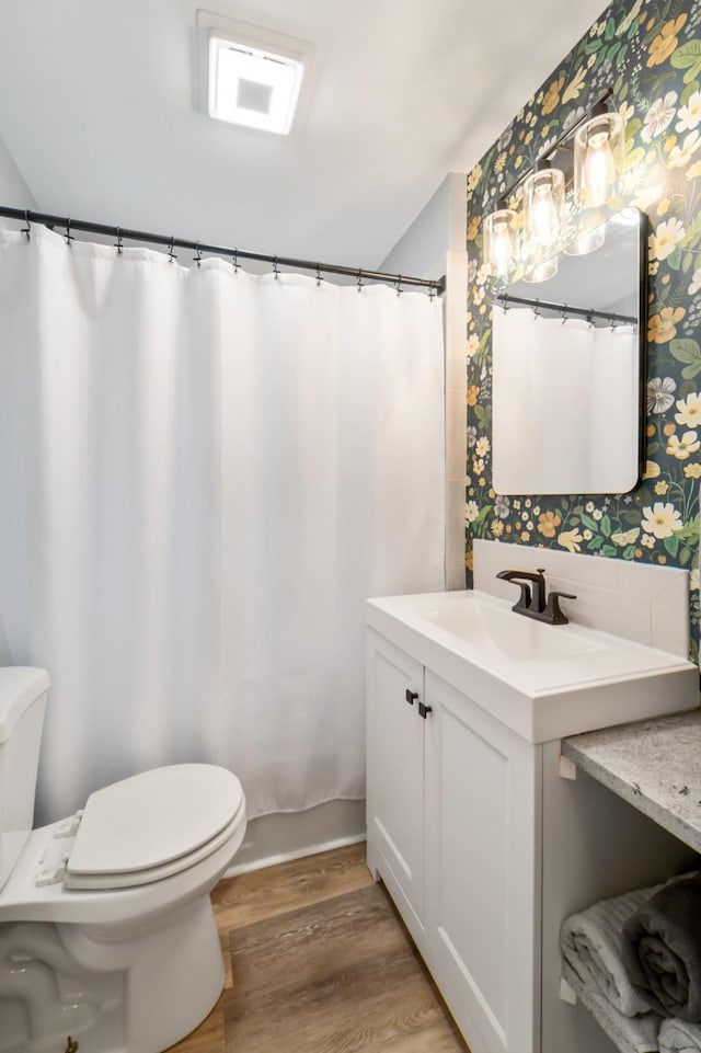 1516 57th Pl, Des Moines, IA 50311 - bathroom with wallpapered walls, toilet, wood finished floors, vanity, and a shower with curtain