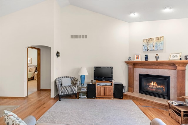 6814 Aubrey Ct, Johnston, IA 50131 - living area with arched walkways, a tiled fireplace, wood finished floors, baseboards, and high vaulted ceiling