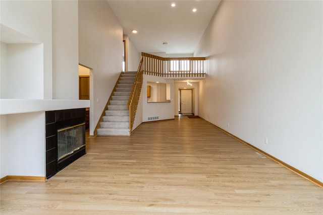 4400 Ep True Pkwy Unit 4, West Des Moines, IA 50265 - unfurnished living room featuring light wood-style floors, recessed lighting, a tiled fireplace, stairs, and a towering ceiling