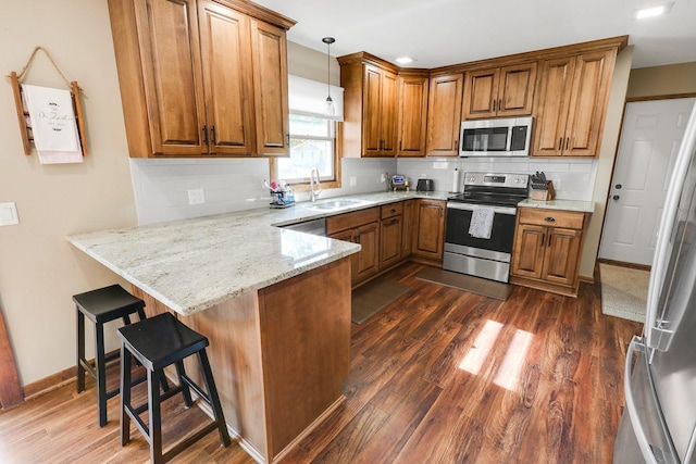 216 E 9th St, Pella, IA 50219 - kitchen with appliances with stainless steel finishes, brown cabinets, a peninsula, a sink, and light stone counters