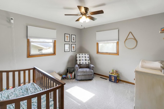 216 E 9th St, Pella, IA 50219 - carpeted bedroom featuring baseboards, a nursery area, and a ceiling fan
