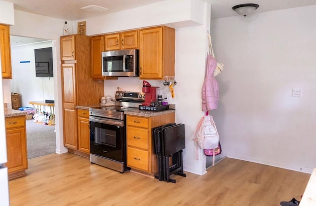 2326 E 39th Ct, Des Moines, IA 50317 - kitchen featuring stainless steel appliances, light wood-style flooring, brown cabinetry, and light stone countertops