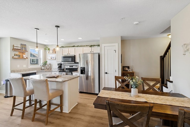 247 Red Oak Ct, Norwalk, IA 50211 - kitchen featuring appliances with stainless steel finishes, a center island, light wood-style floors, white cabinetry, and a breakfast bar area