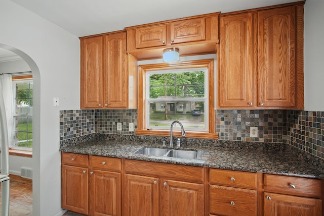 2620 Arnold Rd, Des Moines, IA 50310 - kitchen with a sink, arched walkways, dark stone counters, backsplash, and brown cabinets