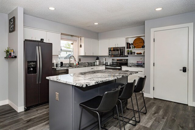 405 Joy Cir, Gilbert, IA 50105 - kitchen with appliances with stainless steel finishes, dark wood-type flooring, a breakfast bar area, white cabinets, and a kitchen island