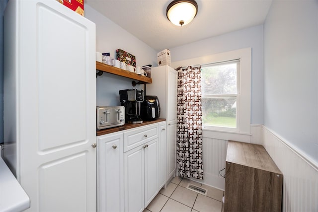 1058 40th St, Des Moines, IA 50311 - kitchen with open shelves, dark countertops, white cabinetry, light tile patterned flooring, and wainscoting