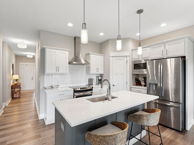 8876 Scarlet Dr, West Des Moines, IA 50266 - kitchen featuring appliances with stainless steel finishes, wall chimney range hood, light wood finished floors, a kitchen bar, and recessed lighting