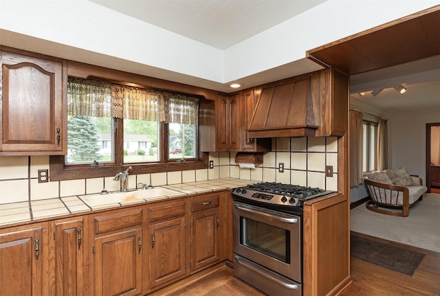 203 11th St, Dallas Center, IA 50063 - kitchen featuring stainless steel gas stove, custom range hood, brown cabinetry, tile countertops, and a sink