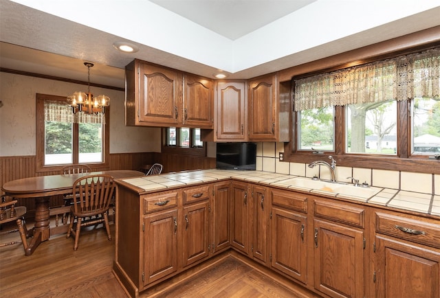 203 11th St, Dallas Center, IA 50063 - kitchen with a wainscoted wall, brown cabinets, a chandelier, a peninsula, and a sink