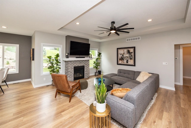16004 Plum Dr, Urbandale, IA 50323 - living area with a raised ceiling, a ceiling fan, light wood-style flooring, a brick fireplace, and baseboards