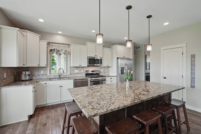 9012 NW 72nd Pl, Johnston, IA 50131 - kitchen featuring appliances with stainless steel finishes, a sink, dark wood-style floors, a breakfast bar area, and a center island