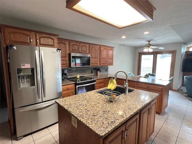 210 E 24th St N, Newton, IA 50208 - kitchen with stainless steel appliances, a sink, a kitchen island with sink, light tile patterned flooring, and brown cabinetry