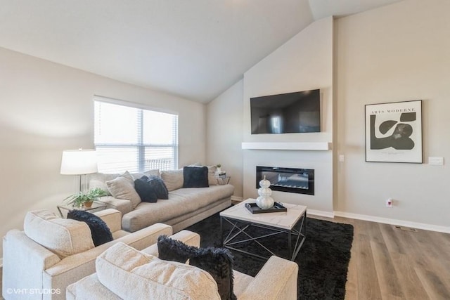14225 Walnut Meadows Dr, Urbandale, IA 50323 - living area featuring wood finished floors, vaulted ceiling, a glass covered fireplace, and baseboards
