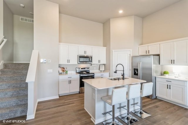 14225 Walnut Meadows Dr, Urbandale, IA 50323 - kitchen with appliances with stainless steel finishes, a sink, a towering ceiling, dark wood finished floors, and white cabinets