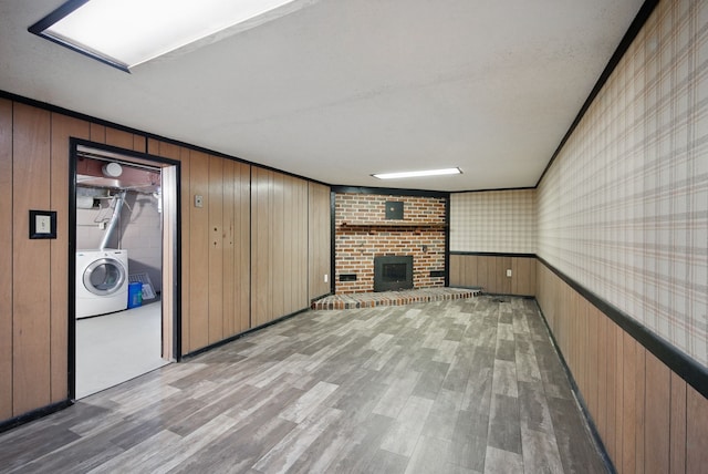 7105 Madison Ave, Urbandale, IA 50322 - unfurnished living room with washer / dryer, light wood-type flooring, a brick fireplace, wood walls, and wallpapered walls