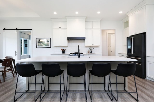 8019 NW 106th Ct, Johnston, IA 50131 - kitchen with black fridge, custom exhaust hood, a center island with sink, light countertops, and recessed lighting