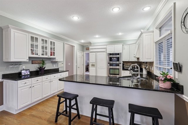 6909 Capitol View Ct, Johnston, IA 50131 - kitchen with stainless steel double oven, a sink, a peninsula, white cabinetry, and glass insert cabinets