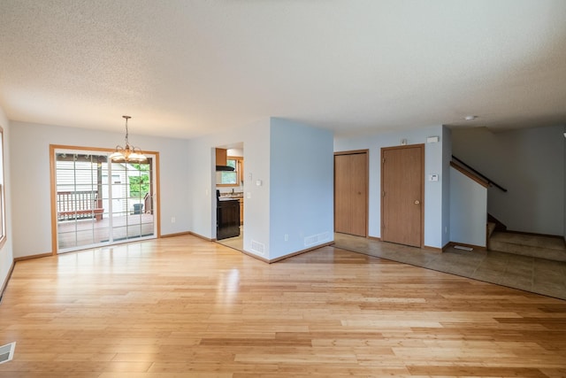 1540 8th St, Des Moines, IA 50314 - unfurnished living room with light wood-style flooring, stairs, a chandelier, and a textured ceiling