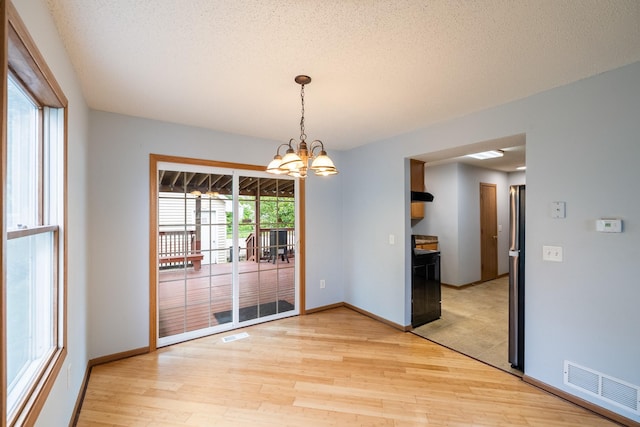 1540 8th St, Des Moines, IA 50314 - unfurnished dining area with light wood finished floors, a chandelier, and a textured ceiling