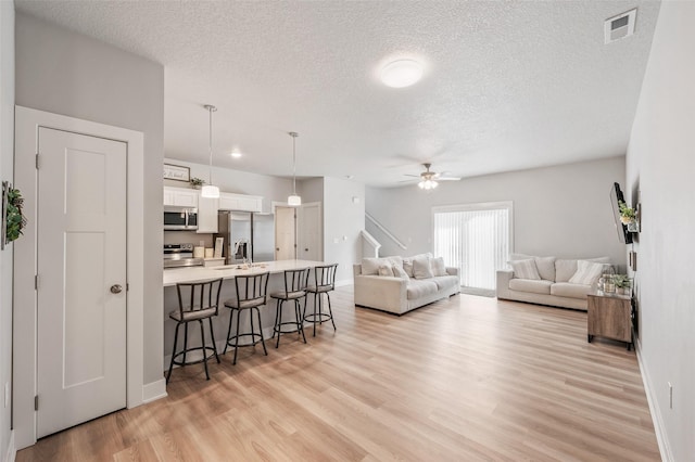 714 Umbra Pl, Norwalk, IA 50211 - living room featuring a textured ceiling, light wood-type flooring, ceiling fan, baseboards, and stairs