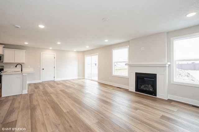 2925 6th Ave SW, Altoona, IA 50009 - unfurnished living room featuring a sink, a glass covered fireplace, light wood finished floors, recessed lighting, and baseboards