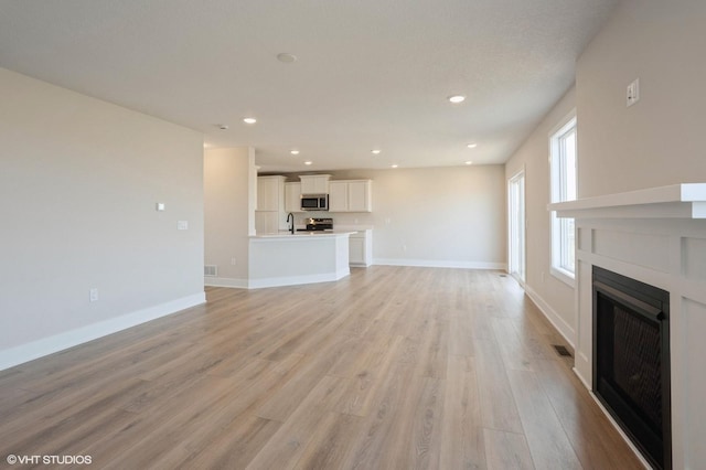 3010 6th Ave SW, Altoona, IA 50009 - unfurnished living room featuring a fireplace, light wood-style floors, recessed lighting, baseboards, and a sink