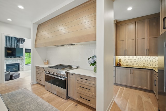 1004 NW Hugg Dr, Polk City, IA 50226 - kitchen with range with two ovens, light wood-style flooring, decorative backsplash, recessed lighting, and a glass covered fireplace