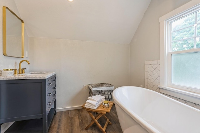 140 N 7th St, Carlisle, IA 50047 - bathroom featuring vaulted ceiling, vanity, a freestanding bath, and wood finished floors