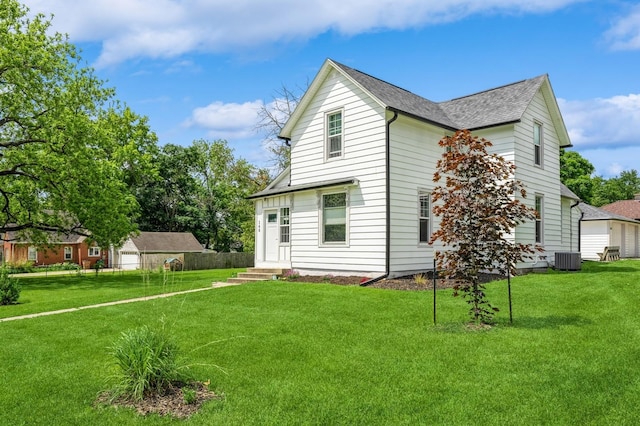 140 N 7th St, Carlisle, IA 50047 - view of side of property with central AC unit, a yard, a shingled roof, and an outdoor structure
