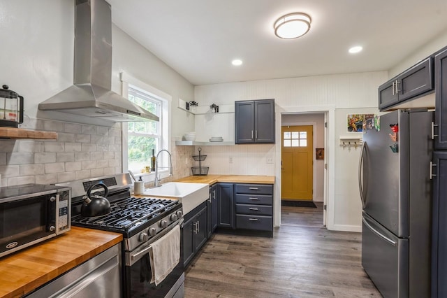 140 N 7th St, Carlisle, IA 50047 - kitchen featuring butcher block countertops, appliances with stainless steel finishes, wall chimney range hood, open shelves, and a sink