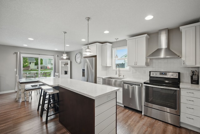 603 Elm Ct, Dallas Center, IA 50063 - kitchen featuring stainless steel appliances, wall chimney range hood, a kitchen island, a breakfast bar area, and dark wood-style floors