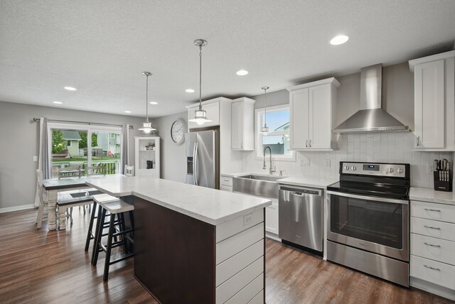 603 Elm Ct, Dallas Center, IA 50063 - kitchen with stainless steel appliances, wall chimney exhaust hood, a kitchen island, a breakfast bar area, and dark wood-style floors