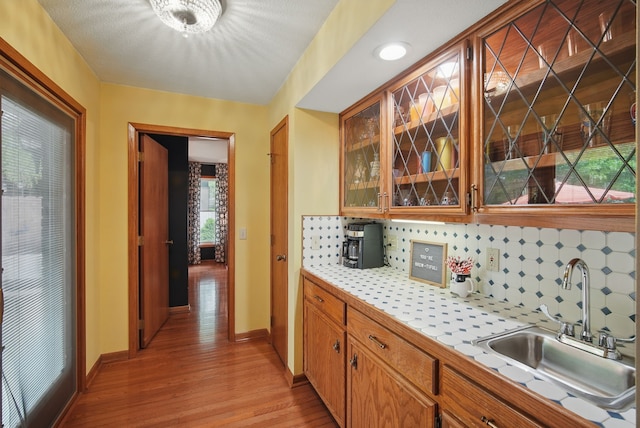 711 36th St, West Des Moines, IA 50265 - kitchen with a sink, tile countertops, light wood-style floors, tasteful backsplash, and glass insert cabinets