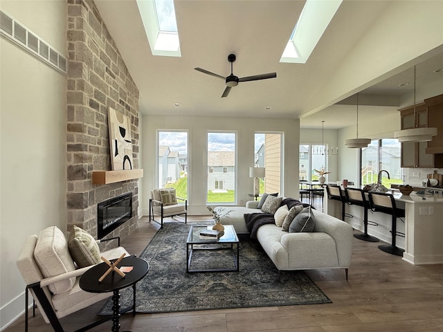 18109 Tanglewood Dr, Clive, IA 50325 - living room featuring a skylight, a stone fireplace, ceiling fan, wood finished floors, and high vaulted ceiling