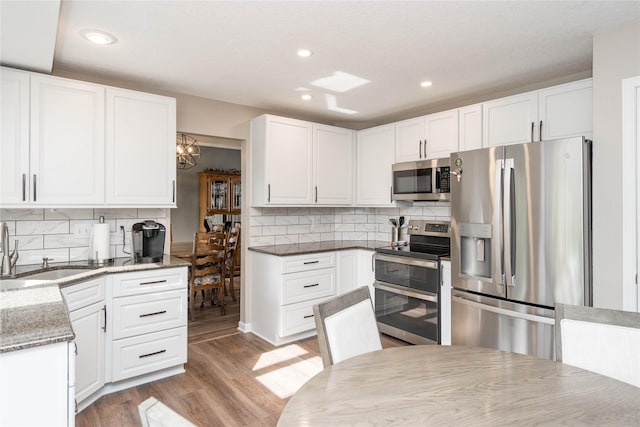 6640 Monticello Ct, Johnston, IA 50131 - kitchen with stainless steel appliances, a sink, light wood-style flooring, decorative backsplash, and white cabinets