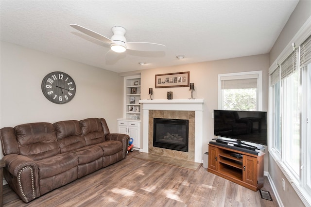 6640 Monticello Ct, Johnston, IA 50131 - living room featuring a ceiling fan, wood finished floors, a tiled fireplace, built in features, and a textured ceiling