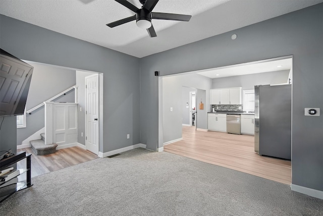 3421 Amherst St, Des Moines, IA 50313 - unfurnished living room featuring ceiling fan, light colored carpet, stairs, baseboards, and light wood-style flooring