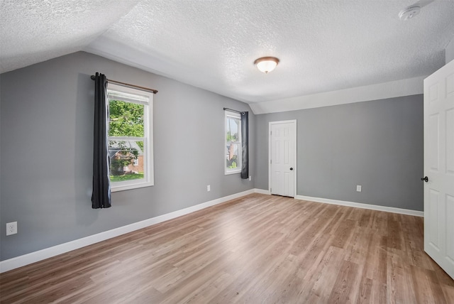 3421 Amherst St, Des Moines, IA 50313 - unfurnished bedroom featuring a textured ceiling, lofted ceiling, light wood finished floors, multiple windows, and baseboards