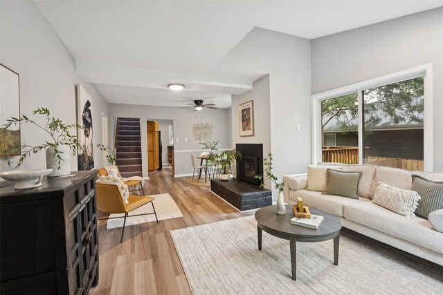 827 40th Pl, Des Moines, IA 50312 - living room featuring light wood finished floors, a ceiling fan, a glass covered fireplace, and stairway