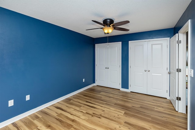 196 79th St, West Des Moines, IA 50266 - unfurnished bedroom featuring two closets, baseboards, light wood-style flooring, a textured ceiling, and ceiling fan