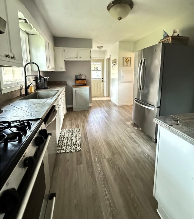 1541 42nd St, Des Moines, IA 50311 - kitchen with appliances with stainless steel finishes, tile countertops, wood finished floors, white cabinetry, and extractor fan