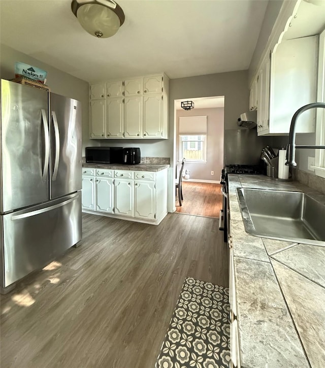 1541 42nd St, Des Moines, IA 50311 - kitchen featuring appliances with stainless steel finishes, tile countertops, white cabinetry, dark wood-style floors, and under cabinet range hood