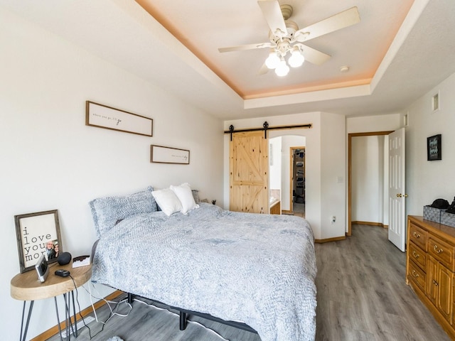 5213 SE 30th St, Des Moines, IA 50320 - bedroom featuring a tray ceiling, light wood-style floors, a barn door, baseboards, and ceiling fan